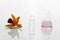 Orange orchid flower with glass vial and flask with pink solution on white science cosmetic laboratory background