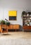 Orange painting above wooden cupboard in retro flat interior with armchair and plants. Real photo