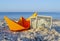 Orange paper boat and two paper dollar bills half buried in sand on sandy beach