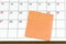 Orange paper sticky note on calendar. Copy space.