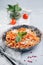 Orange pasta with tomatoes and sauce in a plate on a table.