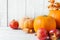 Orange and peachy pumpkins ripe organic red glossy apples pomegranates dry golden leaves on white wood background. Thanksgiving