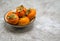 Orange persimmons in a small bowl on a marble counter top