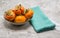 Orange persimmons in a small bowl next to a linen napkin on a marble counter top