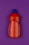 Orange plastic bottle of dishwashing liquid on purple background close-up