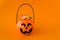 Orange plastic candy basket in the shape of a pumpkin jackolantern on a orange background. Place for your text, layout