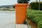 An orange plastic wheeled recycling rubbish bin beside the road