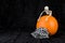 Orange pumpkin on black velvet background, fabric skeleton pattern face mask, plastic skeleton, celebrating Halloween