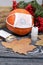 Orange pumpkin in a medical mask. Lies on black pine boards. Nearby is a bouquet of dried grass and mountain ash. There is a