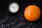 Orange pumpkin and traditional clock on a black velvet background, fall time change