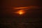 Orange and red sunset over the sea with clouds surrounding the sun and choppy sea