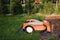 An orange robotic lawn mower stands on the base and is charged from electricity in the courtyard