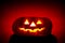 Orange scarry pumpkin with burning eyes on red