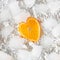 orange slice of fruit in shape of frozen heart. sliver iced background.cold white and vivid orange color.aesthetic flat lay