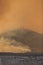 Orange smoke from a large wildfire over a partially burned hill in the desert