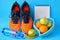 Orange sneakers, measuring tape, bottle of water, notepad and heart shaped bowl of fruit on blue background