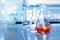 Orange solution in science glass flask in blue chemistry school laboratory background