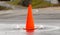 An orange street cone between two small fountains of water