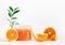 Orange sugar scrub setting with halved and sliced orange fruits and green leaves at white background. Healthy skin care treatment