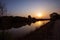 Orange sun rising over river water on dark silhouette edges