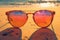 Orange sunglasses on sandy shores frame vibrant ocean sunset scene