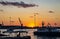 Orange sunset on the black sea in the port with floating yachts and palm trees in the distance against the setting sun, landscape