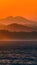 Orange sunset casts warm glow over ocean and mountain vista