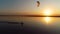 Orange sunset over a lake on which a lonely kitesurfer rushes