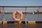 An orange swimming ring on a metal fence on a pedestrian crossing at a wharf beside the river