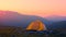 An orange tent stands against the background of a mountain range in the warm sunset light. Hiking in the mountains