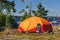 Orange tent, tourist solar panel, sea kayak, coffee maker on the island. Camping equipment, outdoor activities, kayaking