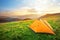 Orange tourist tent in the mountains on a meadow with green grass