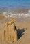orange toy excavator stands on a castle built of coastal sand against the backdrop of the sea