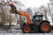 orange tractor with hydraulic lift and a woodcutter with chainsaw working in a tree