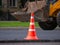 Orange traffic cone on road being repaired. Tractor is driving on background