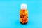 Orange transparent bottle with white cap for medicines filled with different color pills.