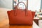 Orange trendy handy leather fashionable women bag on wooden table in coffee cafe