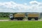 An orange truck with a trailer transports grain along the highway on a beautiful natural landscape. The time of harvesting of