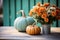 Orange and turquoise pumpkins near flowers on a wood table. Farmhouse autumn centerpiece on blurred backyard background.