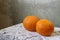 Orange two oranges on a white table cloth hand-knitted by a concrete gray wall in divorces in the loft.