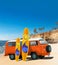 Orange Vintage, Retro, Old-fashioned mini bus van camper VW T2 with surfboard on beach, cliff, palm tree