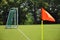 Orange vivid corner flag on fresh green football ground, trees in background, sunny day