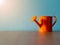 Orange watering cans put on wooden table. the background is turquoise and copy space for content.