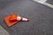 Orange and white reflective street cone flat on the tarmac run over by a vehicle/car