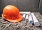 Orange workers helmet on grey wall background. Architectural work place and blueprints.