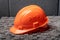Orange workers helmet on grey wall background. Architectural work place and blueprints.