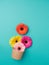 Orange, yellow and pink gerbera flowers coming out of a small biodegradable cardboard bowl opened on plain turquoise background.