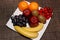 Oranges, apples, grapes, kiwis, cherries, bananas on the white plate on the brown table