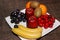 Oranges, apples, grapes, kiwis, cherries, bananas on the white plate on the brown table