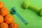 Oranges near dumbbells, measuring tape on green background, top view